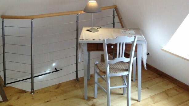 Una habitación pequeña y acogedora con techo de madera, una mesa blanca con lámpara y una silla.