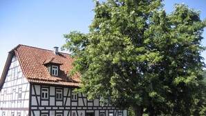 A traditional half-timbered house with a tiled roof, surrounded by a stone wall and a tree. - Landhotel Weisses Ross (Bad Brueckenau)