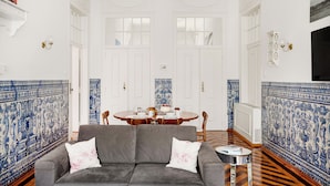 A room with a grey sofa, a dining table with chairs, and a TV mounted on the wall. - Trésor de Fern Apartment (Lisbon)