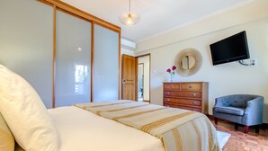 Een slaapkamer met een bed, een dressoir, een stoel, een televisie en een spiegel.