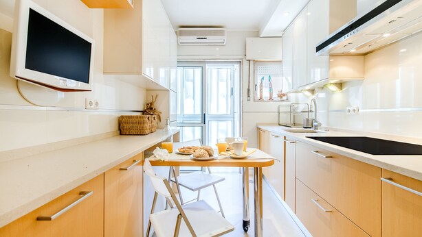 Een moderne keuken met een eettafel, stoelen en een aan de muur bevestigde televisie.