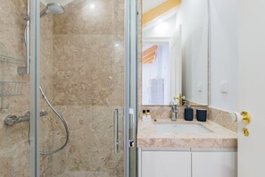 A bathroom with a glass shower enclosure, a sink with a marble countertop, and a large mirror. - Life is Good in Lisbon Baixa Apartment (Lisbon)