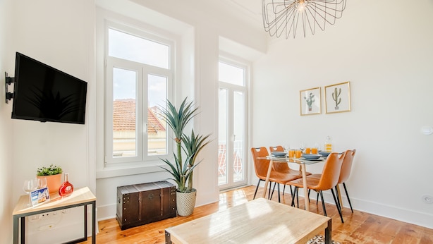 Un salon moderne avec une table en bois, un téléviseur fixé au mur et un coin repas avec des chaises orange.