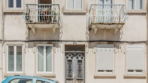 Un immeuble à plusieurs étages doté de balcons, une porte avec un portail en métal et une voiture garée devant.