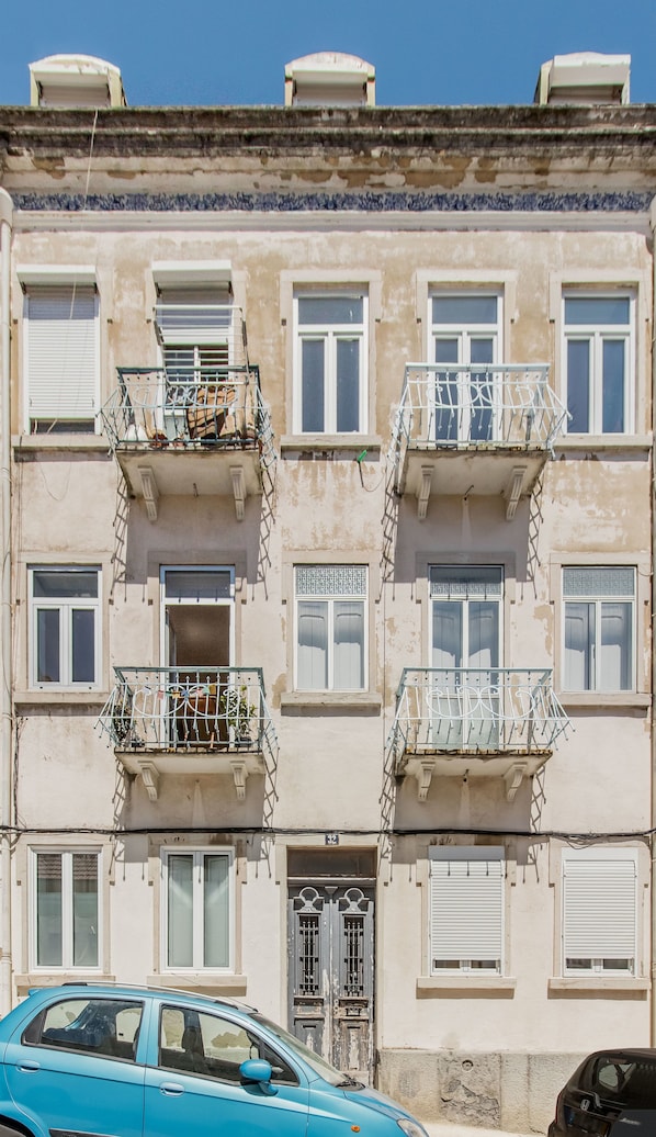 A multi-story building with balconies, a door with a metal gate, and a car parked in front.