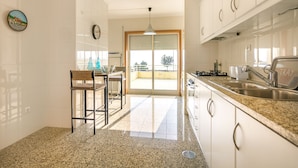 A kitchen with white cabinets, a granite countertop, a sink, and a dining area with a chair and table. - São Félix Ocean Views Apartment (Vila Nova de Gaia)