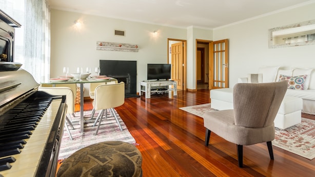 A living room with a piano, a TV, a dining table with chairs, a sofa, and a patterned rug. - São Félix Ocean Views Apartment (Vila Nova de Gaia)