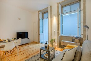 Una sala de estar moderna con un televisor de pantalla plana, una zona de comedor con mesa y sillas, y ventanas amplias con vistas.