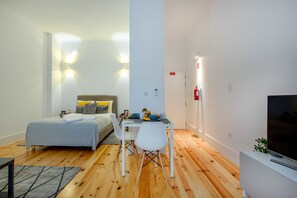 Una habitación moderna y bien iluminada con una cama, una mesa de comedor con sillas, un televisor y una planta pequeña.