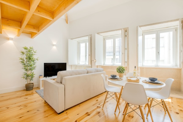 A modern living room with a sofa, dining table, chairs, a TV, and a potted plant.
