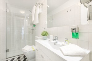 A modern bathroom with a glass shower enclosure, a white sink with a mirror, and a toilet with a white towel.