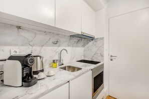 A modern kitchen with white cabinetry, a marble backsplash, a built-in oven, and a coffee machine.