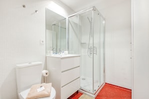Et moderne badeværelse med en brusekabine i glas, en hvid vask med spejl og et toilet.