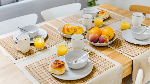 Ein Frühstückstisch reichhaltig gedeckt mit Croissants, Obst, Orangensaft und Kaffeetassen.