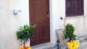 A building with a brown door, a small window with shutters, and two potted plants with yellow flowers. - B&B Tra Gli Ulivi (Rocca San Giovanni)