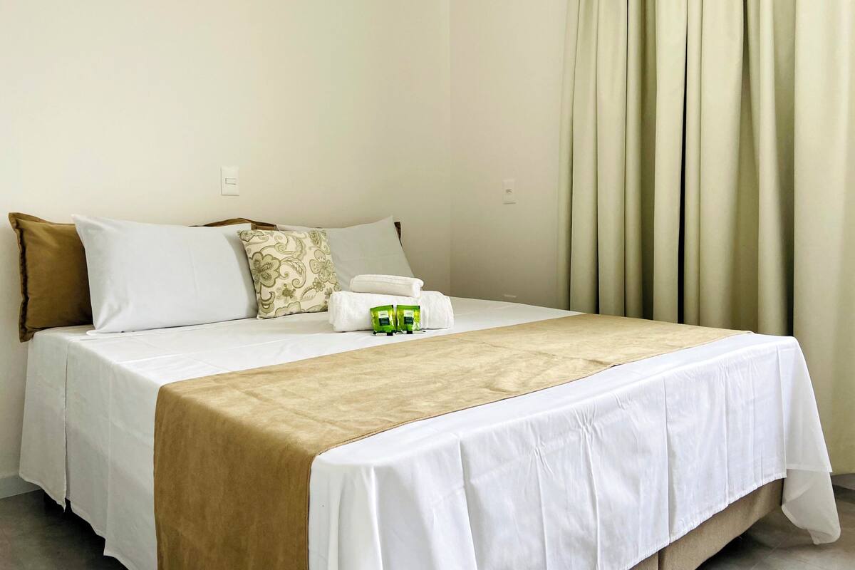 Una habitación de hotel con una cama, almohadas, una mesa con mantel y una cortina.