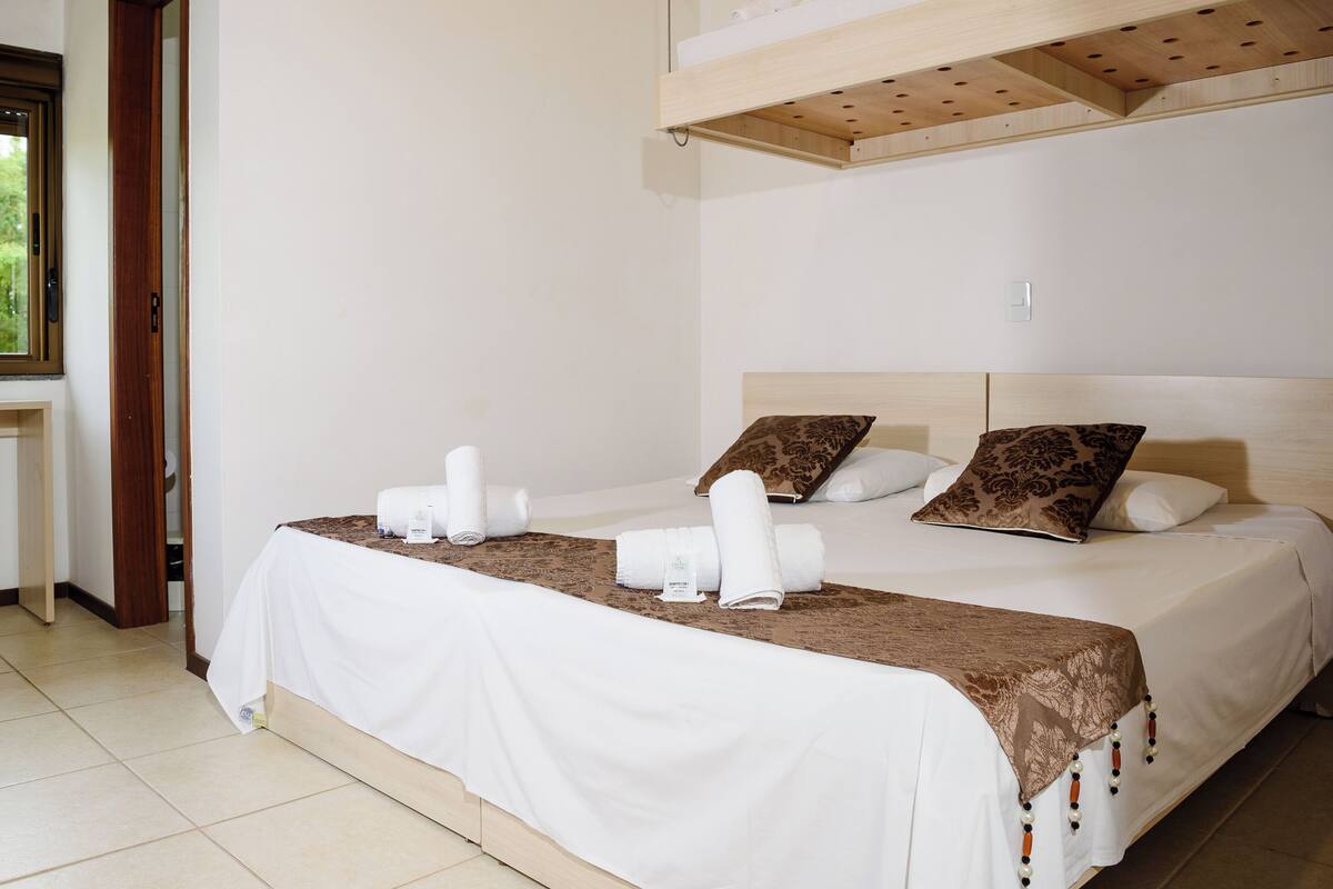 Una habitación de hotel con cama, almohadas, cabecero de madera, ventana y puerta.
