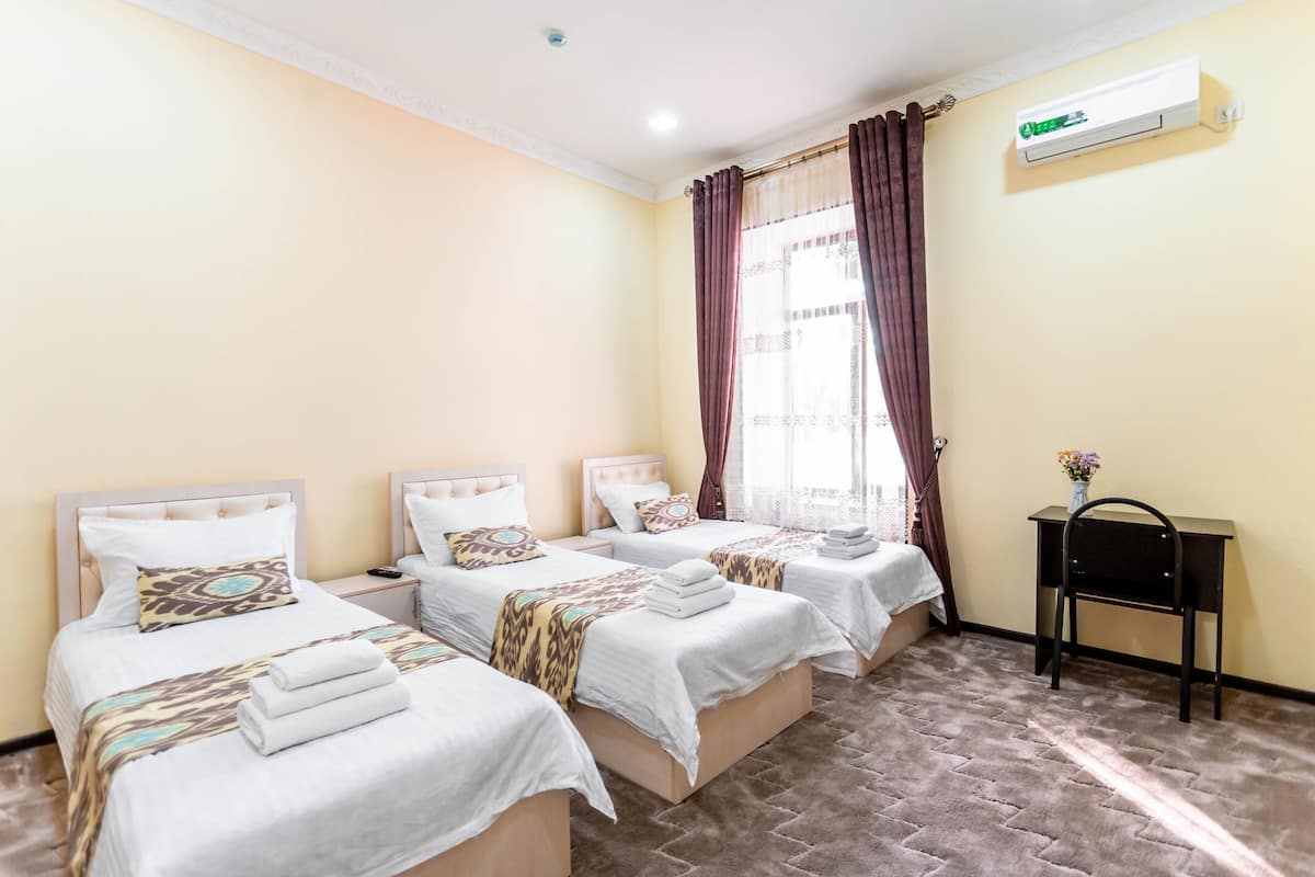 Habitación de hotel con tres camas, un escritorio y un equipo de aire acondicionado.