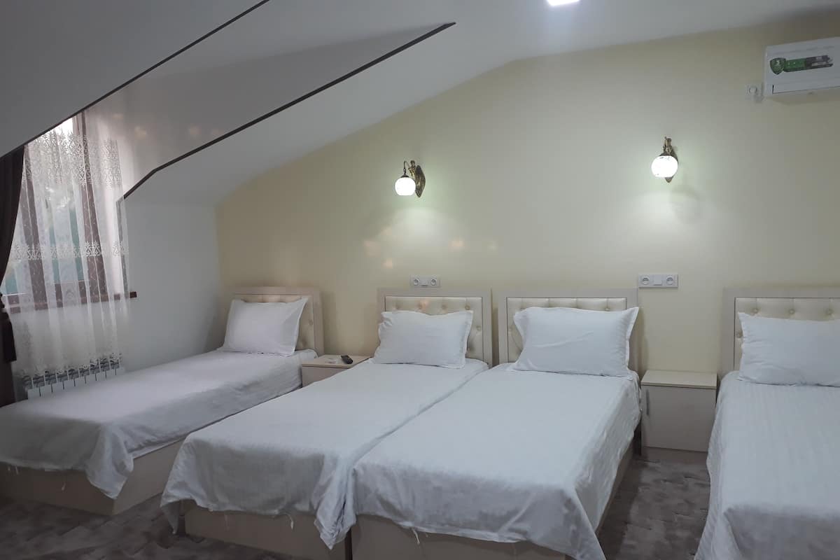 Habitación de hotel con tres camas individuales, un ventilador de techo y dos luces fijadas a la pared.