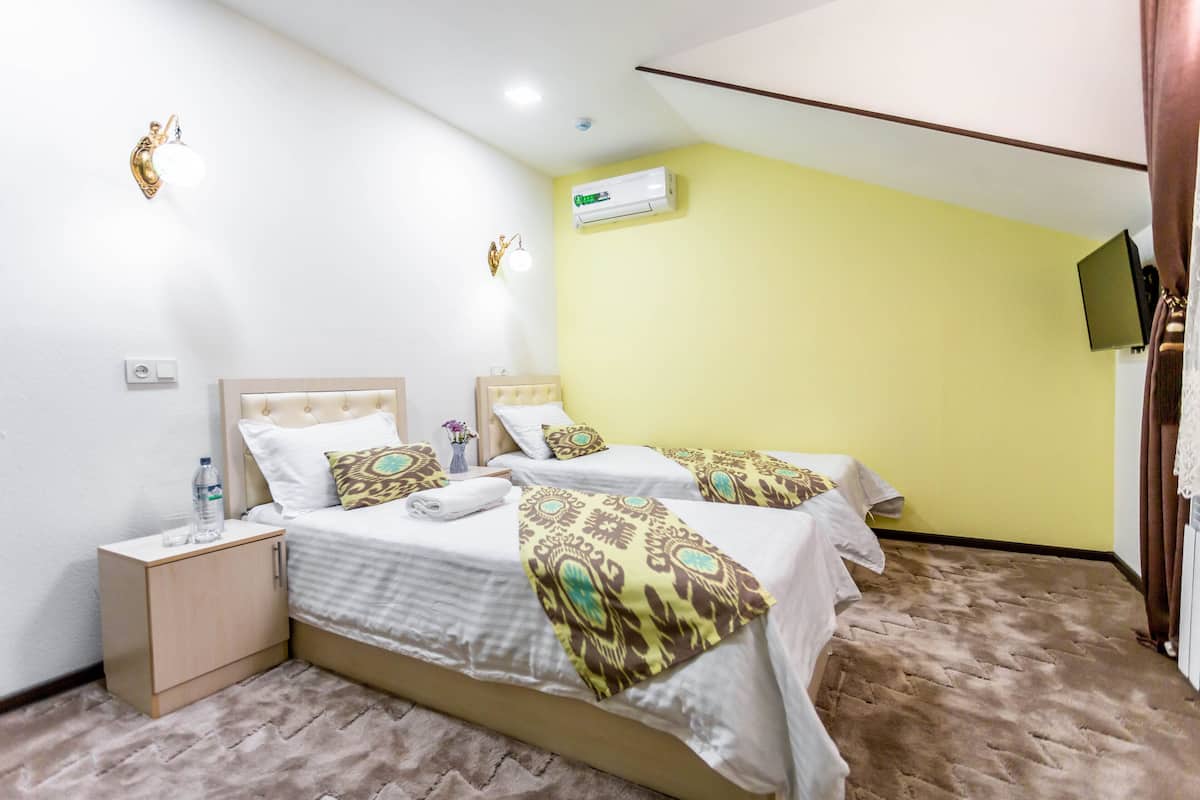 Habitación de hotel con dos camas, una mesita de noche, un equipo de aire acondicionado y un televisor en la pared.