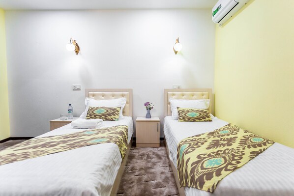 Habitación de hotel con dos camas, mesitas de noche, un jarrón con flores e iluminación en la pared.