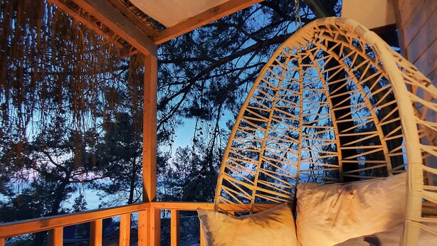 A wooden deck with a hanging chair and a table with a candle. - Rocas Roja Beach Hotel (Fethiye)