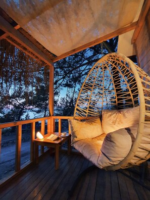 A wooden deck with a hanging chair and a table with a candle. - Rocas Roja Beach Hotel (Fethiye)