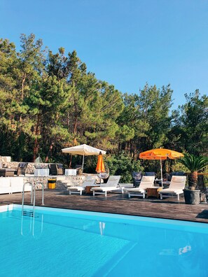 A poolside area with lounge chairs, umbrellas, and a stone wall. - Rocas Roja Beach Hotel (Fethiye)