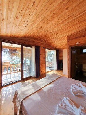 Een houten kamer met een groot bed, schuiframen naar een terras en een open haard.