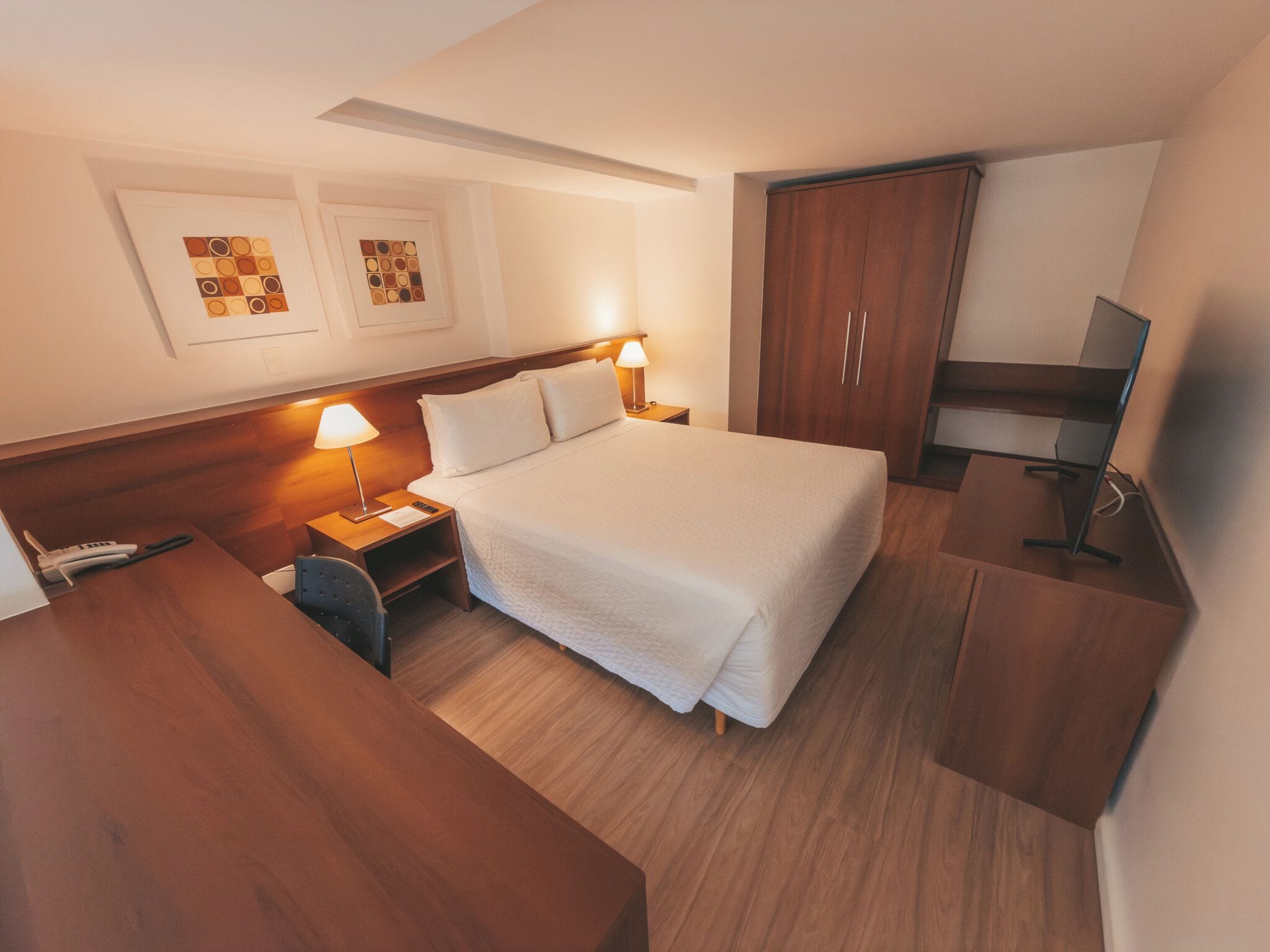 A hotel room with a bed, bedside tables, a desk, a wardrobe, and a television.