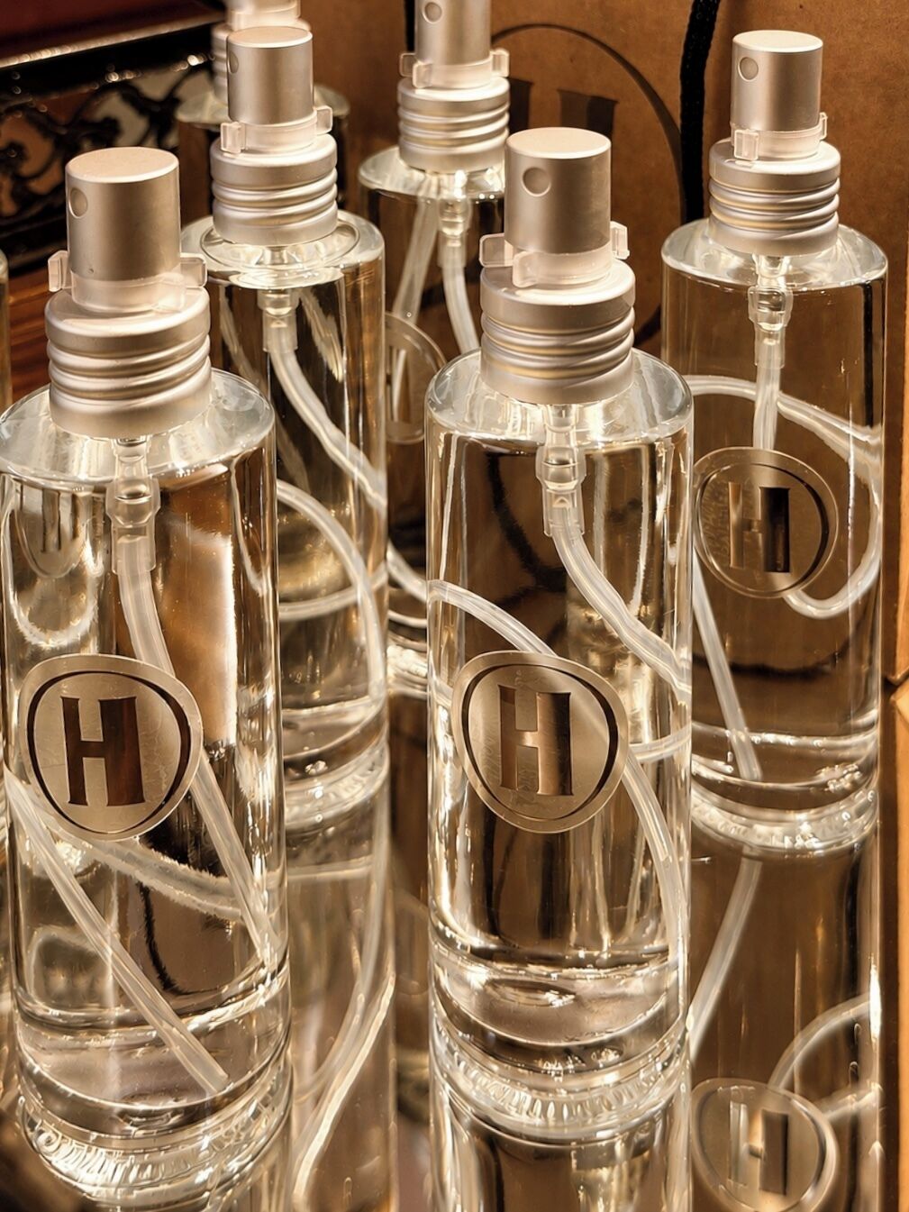 Un conjunto de botellas de vidrio transparente con tapas metálicas, cada una con un llamativo logotipo 'H'.