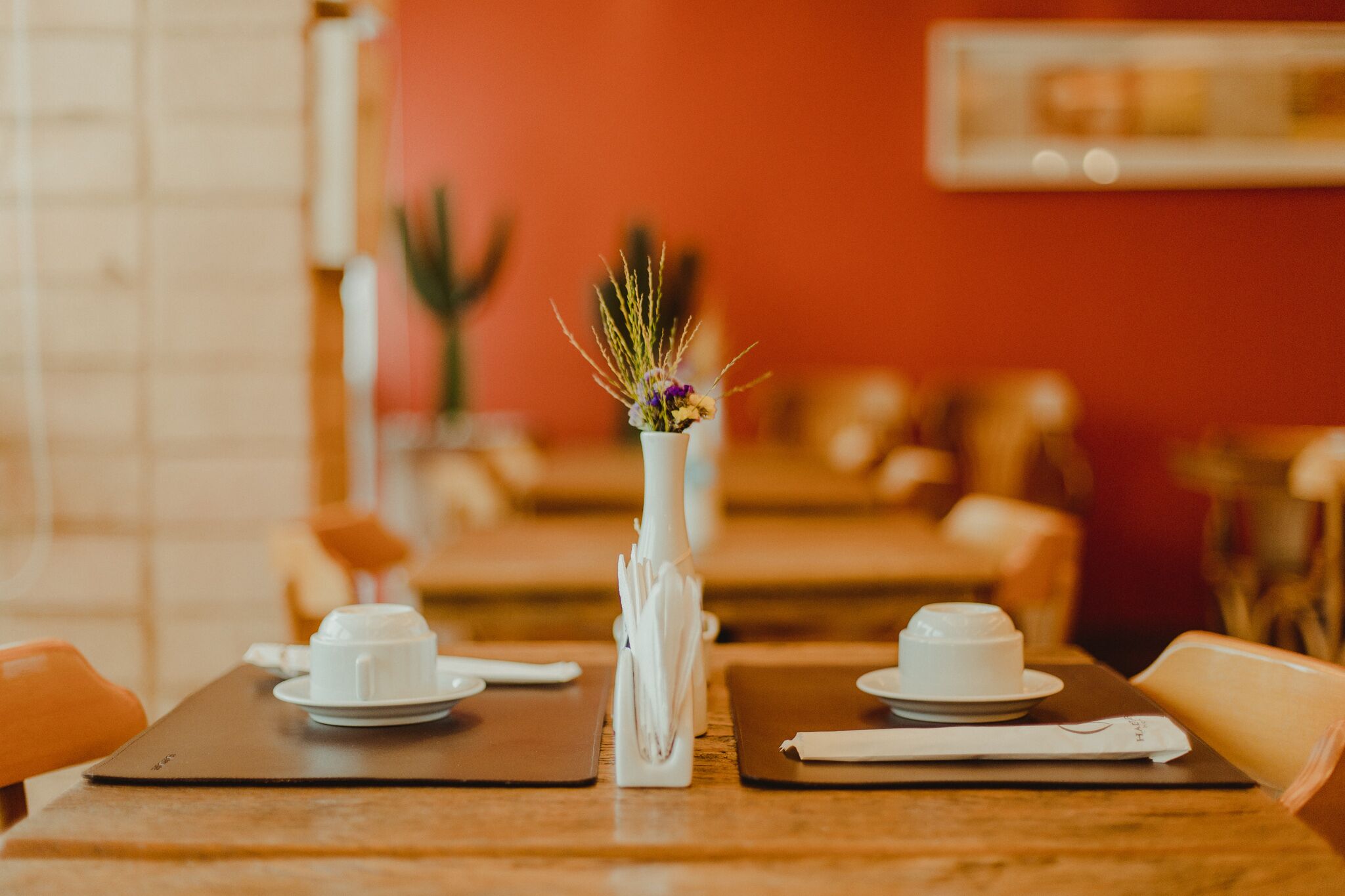 Une table à manger avec de l’assiette blanche, des tasses et un vase contenant des plantes séchées.