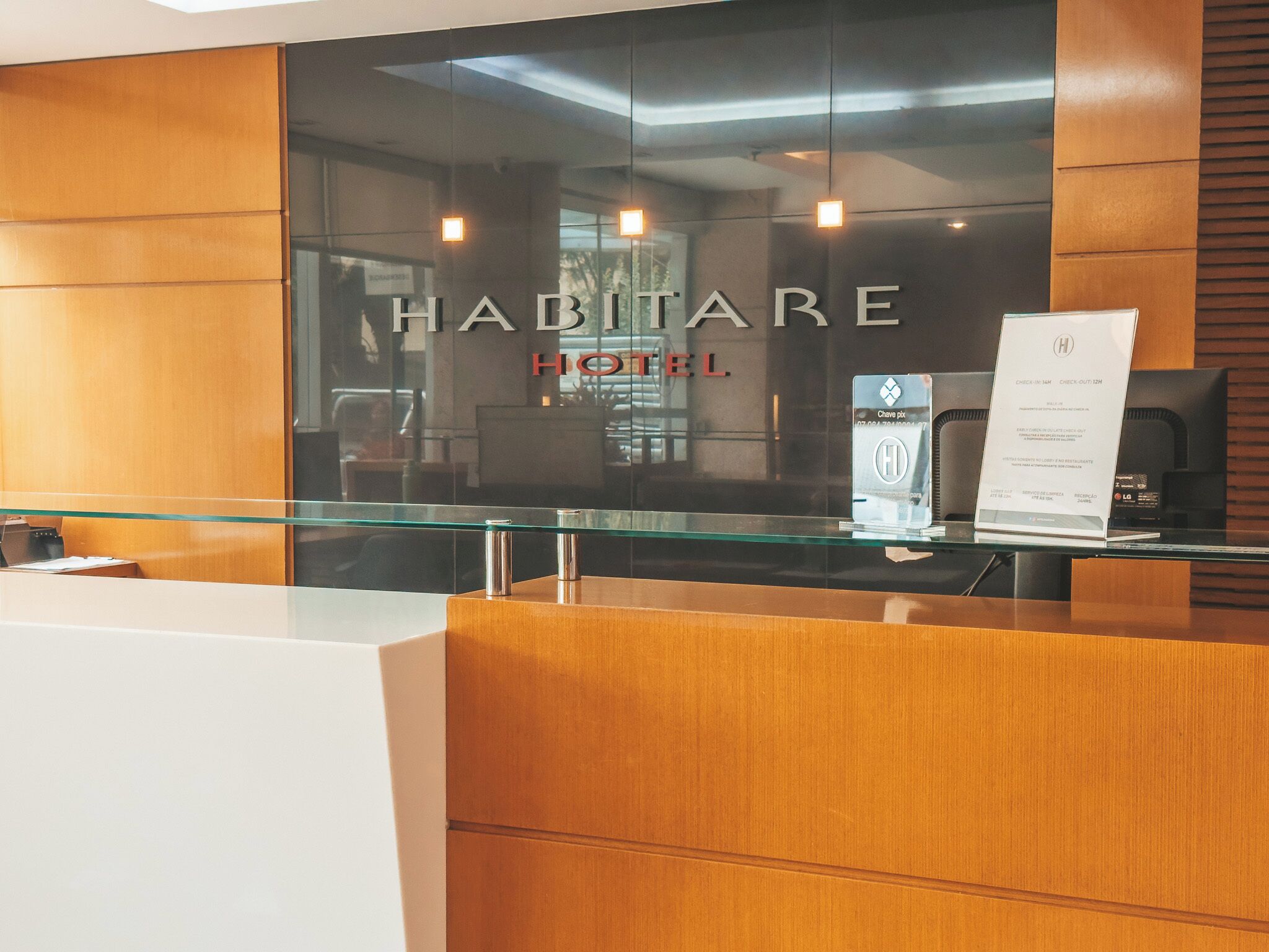 A reception desk with a glass partition, a wooden reception desk, and a sign that reads 'HABITARE HOTEL.'