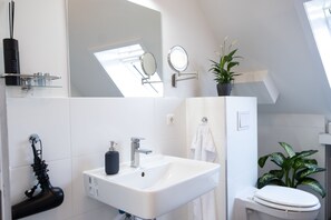 Een moderne badkamer met een wit wastafel, twee spiegels, een handdoekrek, een toilet en een kamerplant.