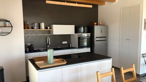 A modern kitchen with a central island, built-in appliances, and a wooden ceiling.
