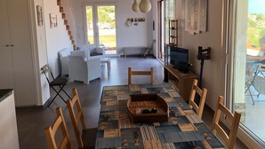 A spacious living area with a sofa, a dining table with chairs, a television, and a staircase leading to another level.