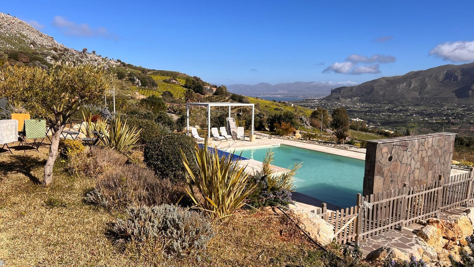 Una piscina con una pergola, circondata da vegetazione arida e uno sfondo montuoso.