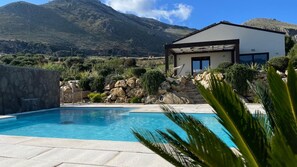 Une piscine avec une vue sur les montagnes, une maison moderne et un mur en pierre.