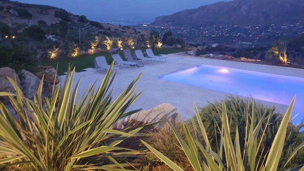 A pool with lounge chairs, surrounded by desert vegetation and a view of a cityscape in the background.