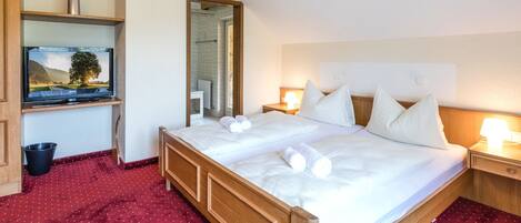 A hotel room with a large bed, a TV on a shelf, a mirror, and a red carpet.