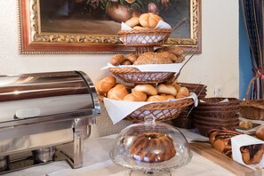 A buffet setup with a coffee maker, baskets of bread, and a covered dessert. - Hotel Wiesenhof (Mieders)