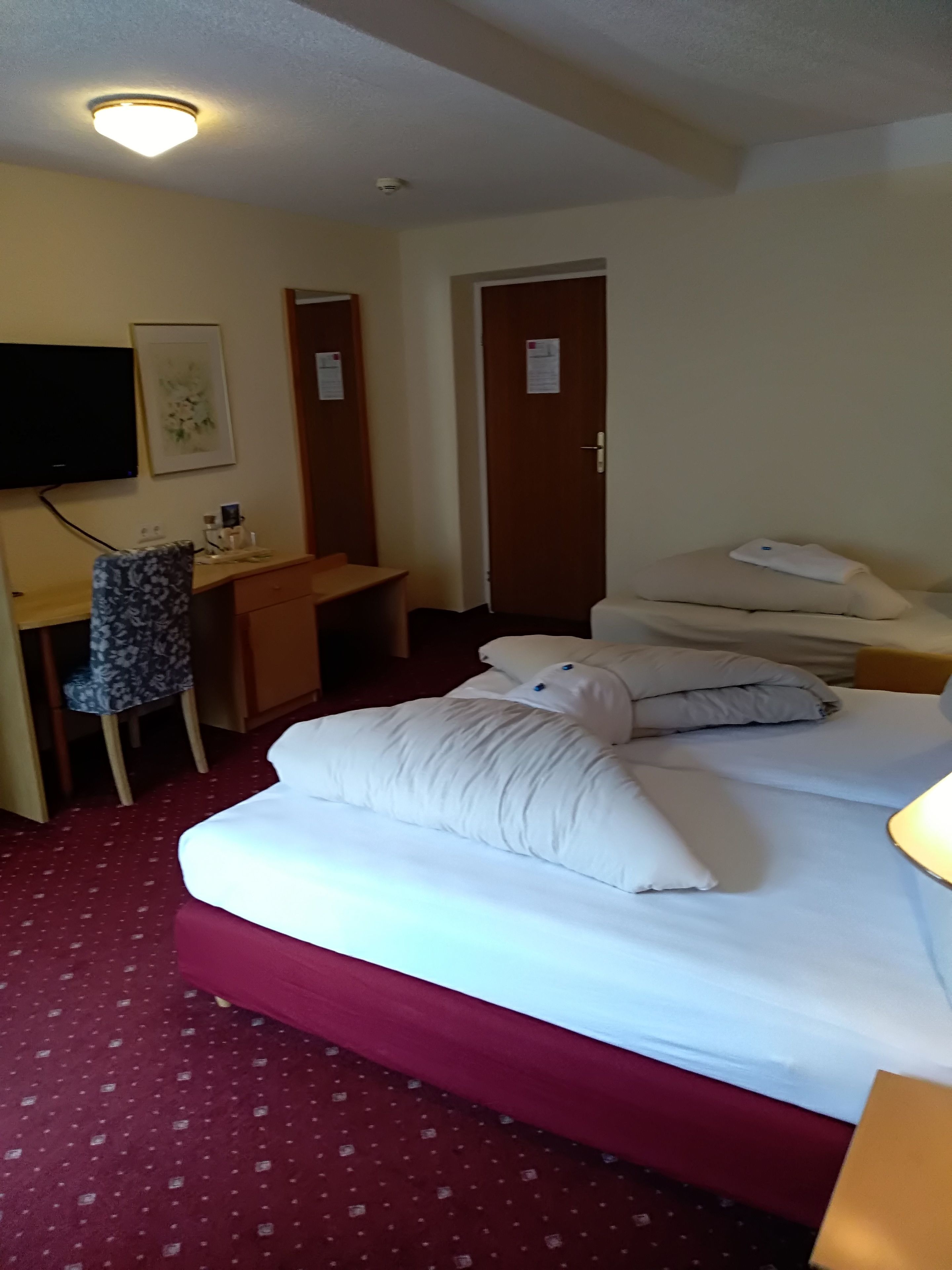 A hotel room with a bed, a desk, a chair, a television, and a door.