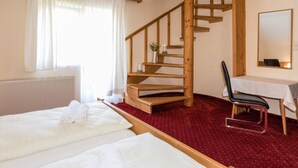 Une chambre d’hôtel avec un escalier en colimaçon en bois, un lit avec du linge de maison blanc, une petite table avec une chaise et un grand miroir au mur.