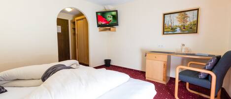 Habitación de hotel con cama, escritorio, silla, televisor y un cuadro en la pared.