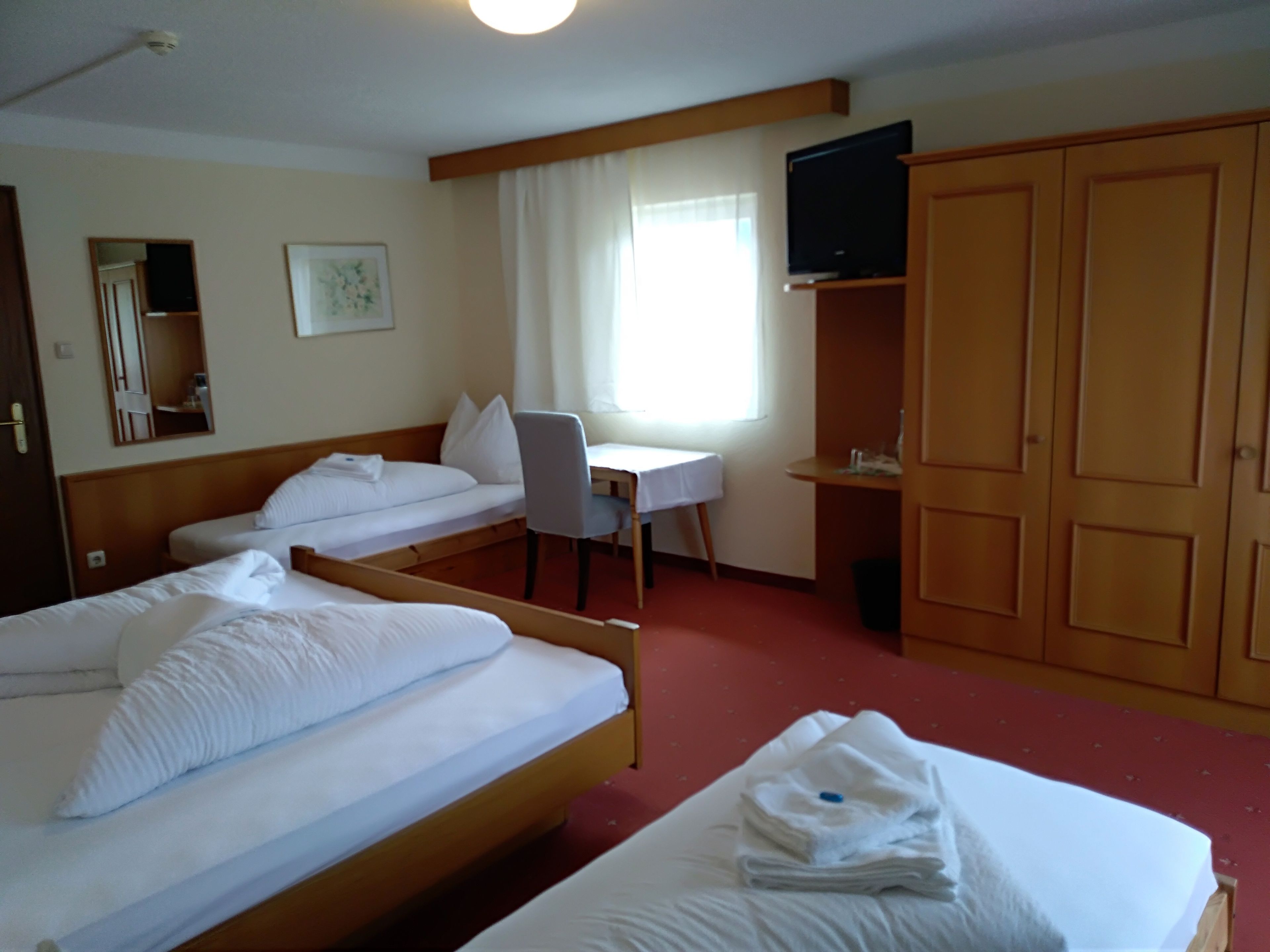 Habitación de hotel con dos camas individuales, un escritorio, una silla, un televisor y un armario.