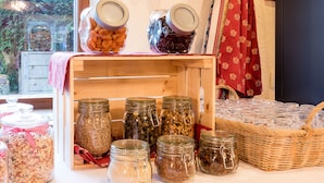 Une variété de bocaux en verre, dotés de couvercles, sont disposés sur une table en bois. Certains contiennent des céréales et des graines, et un panier en osier contient des bocaux en verre vides.