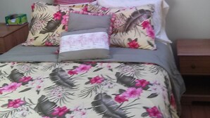 A bedroom with a bed, floral bedspread, and a tapestry with tropical and floral designs.