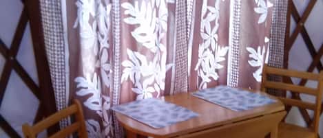 A wooden table with two chairs, a patterned curtain, and a lattice wall.