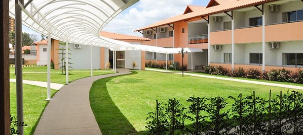 A building with a covered walkway, a well-maintained lawn, and a multi-story structure with balconies.