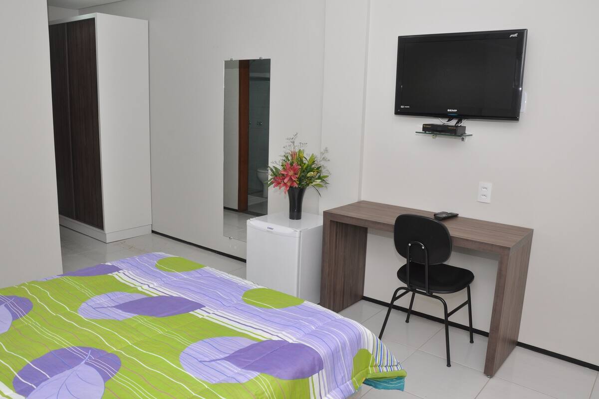 Een hotelkamer met een bed, een bureau, een stoel, een televisie en een kleine koelkast.